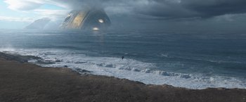Movie still from “Eternals” (2021), directed by Chloé Zhao – A man surfing in the ocean on a cloudy day; Extreme Wide shot, High angle