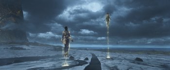 Movie still from “Eternals” (2021), directed by Chloé Zhao – A man standing on top of a rock next to another man; Wide shot, Low angle