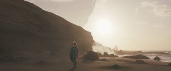 Movie still from “Eternals” (2021), directed by Chloé Zhao – A person walking on a beach near a mountain; Extreme Wide shot, Low angle