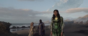 Movie still from “Eternals” (2021), directed by Chloé Zhao – A group of people standing next to each other on a beach; Medium shot, Low angle