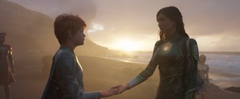 Movie still from “Eternals” (2021), directed by Chloé Zhao – A woman and a boy holding hands on the beach; Medium shot, Over the shoulder angle