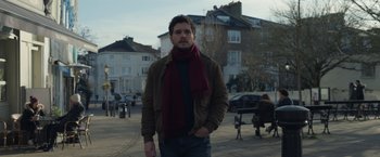 Movie still from “Eternals” (2021), directed by Chloé Zhao – A man wearing a jacket and a red scarf; Medium shot, Low angle