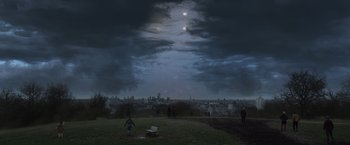 Movie still from “Eternals” (2021), directed by Chloé Zhao – People are standing on a grassy hill under a cloudy sky; Extreme Wide shot, High angle