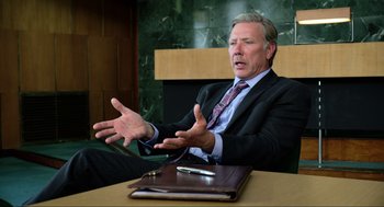 Movie still from “Eurovision Song Contest: The Story of Fire Saga” (2020), directed by David Dobkin – A man in a suit and tie sitting in front of a table; Medium shot, Over the shoulder angle