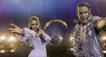 Movie still from “Eurovision Song Contest: The Story of Fire Saga” (2020), directed by David Dobkin – A woman and a man are singing into a microphone; Medium shot, Low angle