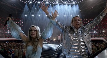 Movie still from “Eurovision Song Contest: The Story of Fire Saga” (2020), directed by David Dobkin – A man and a woman are waving their hands in the air in front of a stage; Medium shot, Low angle