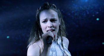 Movie still from “Eurovision Song Contest: The Story of Fire Saga” (2020), directed by David Dobkin – A woman is singing into a microphone; Close Up shot, Over the shoulder angle