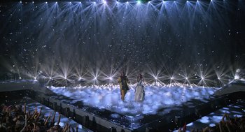 Movie still from “Eurovision Song Contest: The Story of Fire Saga” (2020), directed by David Dobkin – A couple of people are standing on a stage in front of lights; Extreme Wide shot, High angle