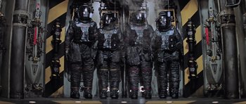 Movie still from “Event Horizon” (1997), directed by Paul W.S. Anderson – A group of men in black suits standing next to each other; Wide shot, Overhead angle