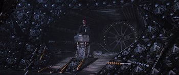 Movie still from “Event Horizon” (1997), directed by Paul W.S. Anderson – A man standing on a stage in front of a microphone; Wide shot, High angle
