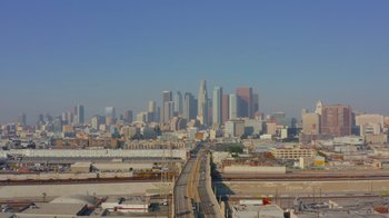 Movie still from “Every Body” (2023), directed by Julie Cohen – An aerial view of a city skyline with a freeway going through it; Extreme Wide shot, High angle