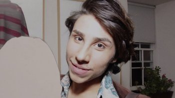 Movie still from “Every Body” (2023), directed by Julie Cohen – A man with long brown hair is smiling for the camera; Extreme Close Up shot, Overhead angle