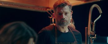 Movie still from “A Taste of Hunger” (2021), directed by Christoffer Boe – A man wearing an apron looking at the camera; Close Up shot, Over the shoulder angle