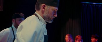Movie still from “A Taste of Hunger” (2021), directed by Christoffer Boe – A man wearing a chef's hat and apron looking down; Close Up shot, Low angle