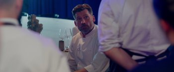 Movie still from “A Taste of Hunger” (2021), directed by Christoffer Boe – A man sitting at a table with a glass of wine in front of him; Close Up shot, Over the shoulder angle