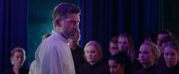 Movie still from “A Taste of Hunger” (2021), directed by Christoffer Boe – A man standing in front of a group of people; Medium shot, Over the shoulder angle