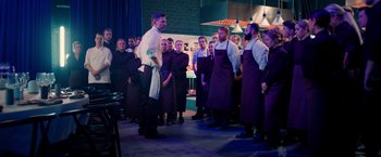 Movie still from “A Taste of Hunger” (2021), directed by Christoffer Boe – A group of people standing in a room with a chef; Wide shot, High angle