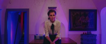 Movie still from “A Taste of Hunger” (2021), directed by Christoffer Boe – A woman sitting on top of a table in a room; Medium shot, Low angle