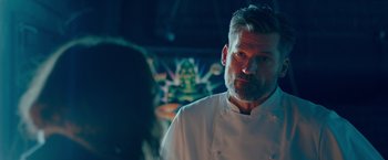 Movie still from “A Taste of Hunger” (2021), directed by Christoffer Boe – A man wearing a chef's outfit in a dark room; Close Up shot, Over the shoulder angle