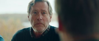 Movie still from “A Taste of Hunger” (2021), directed by Christoffer Boe – An older man looking into a mirror while wearing a sweater; Close Up shot, Over the shoulder angle