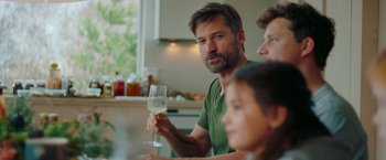 Movie still from “A Taste of Hunger” (2021), directed by Christoffer Boe – A man holding a wine glass in his right hand; Medium shot, Over the shoulder angle