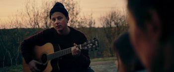 Movie still from “A Taste of Hunger” (2021), directed by Christoffer Boe – A man playing an acoustic guitar in front of another man; Medium shot, Over the shoulder angle