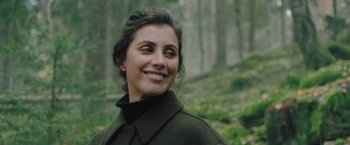 Movie still from “A Taste of Hunger” (2021), directed by Christoffer Boe – A person smiling in a forest; Close Up shot, Over the shoulder angle
