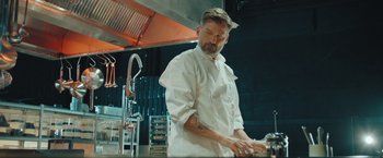 Movie still from “A Taste of Hunger” (2021), directed by Christoffer Boe – A man in a white shirt is in a kitchen; Medium shot, Low angle