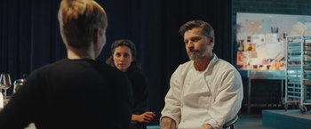 Movie still from “A Taste of Hunger” (2021), directed by Christoffer Boe – A man and two women sitting in front of him; Medium shot, Over the shoulder angle