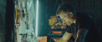 Movie still from “A Taste of Hunger” (2021), directed by Christoffer Boe – A man in a black shirt is playing a video game; Medium shot, Low angle