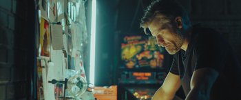 Movie still from “A Taste of Hunger” (2021), directed by Christoffer Boe – A man standing in front of an arcade machine; Close Up shot, Low angle