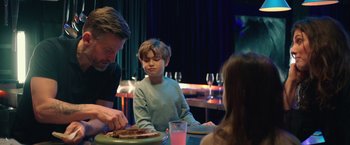 Movie still from “A Taste of Hunger” (2021), directed by Christoffer Boe – A young boy sitting at a table with a plate of food on it; Medium shot, Over the shoulder angle