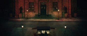 Movie still from “A Taste of Hunger” (2021), directed by Christoffer Boe – A person sitting at a table outside of a building at night; Extreme Wide shot, High angle