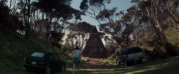 A woman standing in front of a house in the middle of a forest
