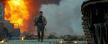 Movie still from “Expend4bles” (2023), directed by Scott Waugh – A man standing in front of a fire and smoke filled sky; Wide shot, Low angle