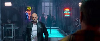 Movie still from “Expend4bles” (2023), directed by Scott Waugh – A man standing in front of a pole in a room; Wide shot, Over the shoulder angle