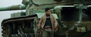 Movie still from “Expend4bles” (2023), directed by Scott Waugh – A man standing in front of an armored vehicle; Medium shot, Over the shoulder angle