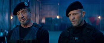 Movie still from “Expend4bles” (2023), directed by Scott Waugh – A man and a woman standing next to each other in a warehouse; Close Up shot, Low angle