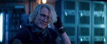 Movie still from “Expend4bles” (2023), directed by Scott Waugh – A man with blonde long hair wearing a black shirt and a pair of black gloves; Close Up shot, Over the shoulder angle