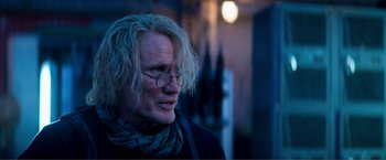 Movie still from “Expend4bles” (2023), directed by Scott Waugh – A man with long blonde hair wearing glasses; Close Up shot, Over the shoulder angle