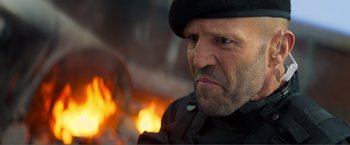 Movie still from “Expend4bles” (2023), directed by Scott Waugh – A person wearing a hat near a fire; Close Up shot, Over the shoulder angle