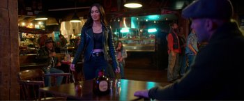 Movie still from “Expend4bles” (2023), directed by Scott Waugh – A woman in a leather jacket standing at a bar; Medium shot, Over the shoulder angle