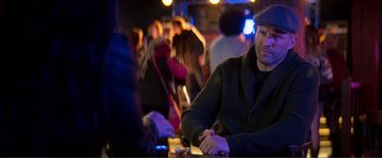 Movie still from “Expend4bles” (2023), directed by Scott Waugh – A man sitting at a table in front of a group of people; Medium shot, Over the shoulder angle