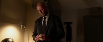 Movie still from “Expend4bles” (2023), directed by Scott Waugh – A bald man in a suit and a tie; Medium shot, Low angle