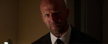 Movie still from “Expend4bles” (2023), directed by Scott Waugh – A bald man in a suit and tie looking at the camera; Close Up shot, Low angle