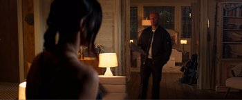 Movie still from “Expend4bles” (2023), directed by Scott Waugh – A man and a woman standing in front of a lamp in a living room; Medium shot, Over the shoulder angle