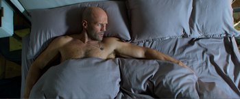 Movie still from “Expend4bles” (2023), directed by Scott Waugh – A man laying in a bed with his arms crossed; Medium shot, Overhead angle