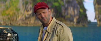 Movie still from “Expend4bles” (2023), directed by Scott Waugh – A man in a red hat and a tan jacket; Close Up shot, Over the shoulder angle