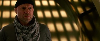 Movie still from “Expend4bles” (2023), directed by Scott Waugh – A man wearing a scarf and a hat is standing in front of a window; Close Up shot, Low angle
