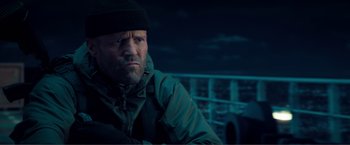 Movie still from “Expend4bles” (2023), directed by Scott Waugh – A man with a beard and a hat is sitting on a boat; Medium shot, Low angle